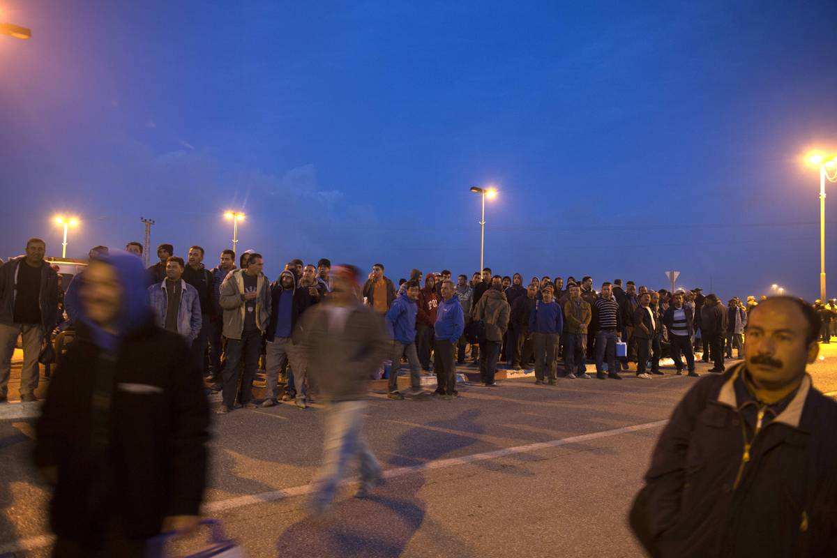 Palestinians wait for a bus to come as a new line is made available by Israel to take Palestinian labourers from the Israeli 