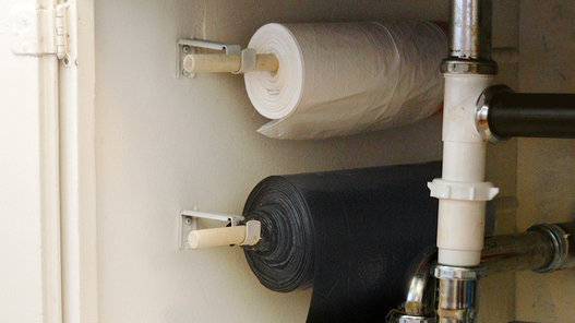 A cardboard box of garbage bags can easily take up half of the under-sink cabinet space. Free up some room by mounting a paper-towel holder to the inside of one cabinet, then use it to hang a roll of trash bags.
