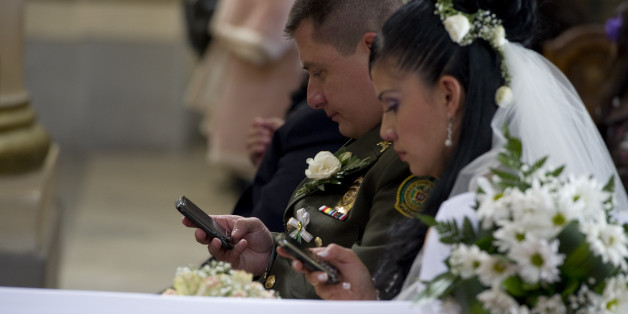 A bride and groom use their mobile phones during a mass wedding of police officers at the Cathedral of Bogota, on December 9, 2011. Ninety-six couples are getting married in the same ceremony. AFP PHOTO/Luis ACOSTA (Photo credit should read LUIS ACOSTA/AFP/Getty Images)