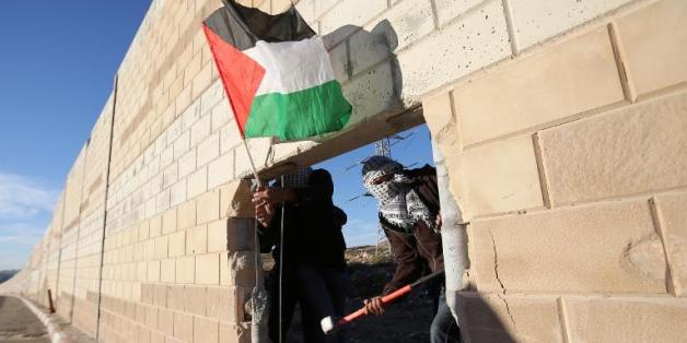 De jeunes Palestiniens brandissent un drapeau palestinien à travers la brèche qu'ils ont creusée dans le mur de séparation entre Israël et le village de Bir Nabala, en Cisjordanie, le 8 novembre 2014