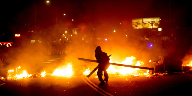 A protester adds wood to a fire burning in Oakland, Calif., on Tuesday, Nov. 25, 2014, a day after the announcement that a grand jury decided not to indict Ferguson police officer Darren Wilson in the fatal shooting of Michael Brown. Protesters briefly shut down two major freeways, vandalized police cars and looted businesses in downtown Oakland, smashing windows at cell phone stores, car dealerships, restaurants and convenience stores on a second night of protests. (AP Photo/Noah Berger)