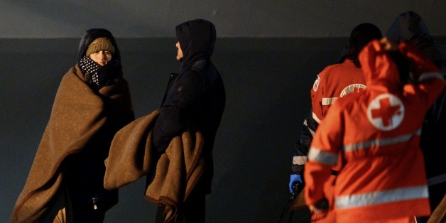 Rescued passengers of the 'Norman Atlantic' ferry stand next to members of the Italian Red Cross after their arrival aboard the Italian Navy ship 'San Giorgio' in Brindisi, southern Italy, on December 30, 2014. The death toll from the ferry disaster in the Adriatic Sea rose to 13 on December 30 as fears mounted that the final count could be much higher. Uncertainty over the scale of the tragedy persisted with Greek and Italian authorities still unable to say with any certainty how many paying passengers were on board the Norman Atlantic when it burst into flames in stormy seas on December 28. AFP PHOTO / FILIPPO MONTEFORTE (Photo credit should read FILIPPO MONTEFORTE/AFP/Getty Images)