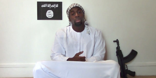 This image made from a video posted online by militants on Sunday, Jan. 11, 2015, shows slain hostage-taker Amedy Coulibaly, who shot a policewoman and four hostages at a kosher grocery in Paris, with a gun in front of an Islamic State emblem as he defends the Paris attacks carried out on the satirical newspaper, police and a Jewish store. At one point in the video, Coulibaly says Charlie Hebdo will be attacked "tomorrow" and that he and the (Said and Cherif Kouachi) brothers were coordinating.