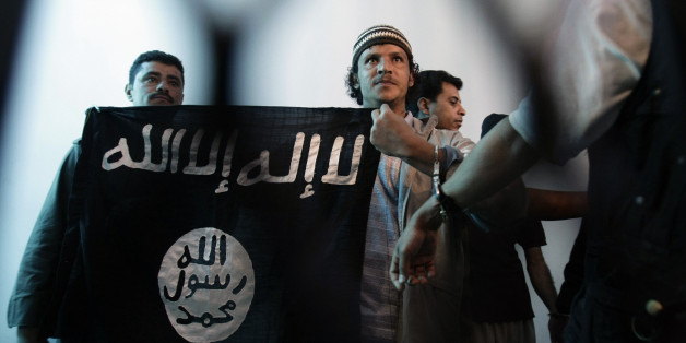 FILE - In this Tuesday, April 23, 2013 file photo, a suspected Yemeni al-Qaida militant, center, holds an Islamist banner as he stands behind bars during a court hearing in state security court in Sanaa, Yemen. Arabic on flag reads, "There is no God but Allah and Mohammed is the messenger of God." Al-Qaida in the Arabian Peninsula, suspected of having ties to the attackers in Paris, has been the most active of the terror network's branches in trying to strike in the West. (AP Photo/Hani Mohamme