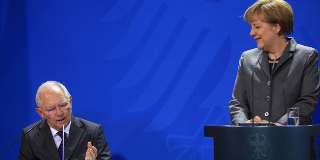 Wolfgang Schaeuble, Germany's finance minister, left, speaks as Angela Merkel, Germany's chancellor, reacts during a news conference to unveil a commemorative two euro German reunification coin at the Chancellery in Berlin, Germany, on Thursday, Jan. 29, 2015. Germany's inflation rate turned negative in January for the first time in more than five years, aggravating a slump in consumer prices in the euro area. Photographer: Krisztian Bocsi/Bloomberg via Getty Images
