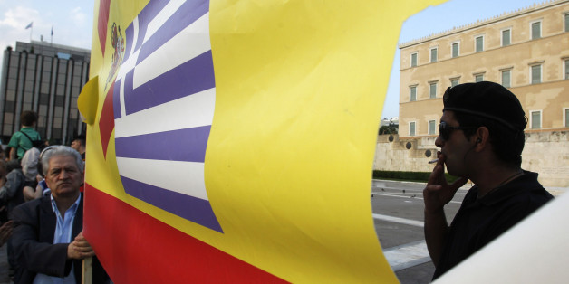 A riot police smokes a cigarette as an elderly man holds a banner with Spanish and Greek flags in front of the Greek Parliament during a peaceful rally for a sixth day, attended by thousands called through a social networking site - modeled on protests by young people in Spain, on Monday, May 30, 2011. Greece could get another euro 20 billion ($28 billion) in aid from its fellow euro countries and raise three times that through new austerity measures such as selling government property, a top Eu