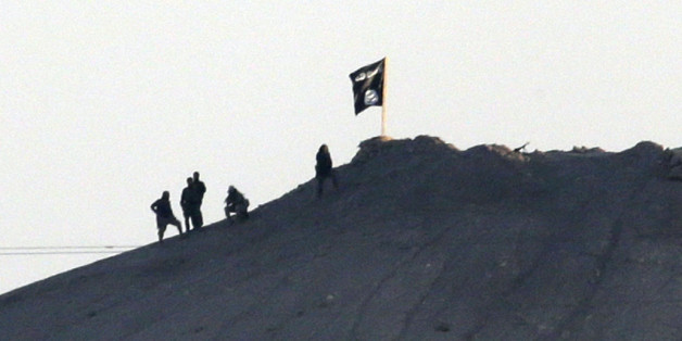 In this image shot with an extreme telephoto lens and through haze from the outskirts of Suruc at the Turkey-Syria border, militants with the Islamic State group are seen after placing their group's flag on a hilltop at the eastern side of the town of Kobani, Syria, where fighting had been intensified between Syrian Kurds and the militants of Islamic State group, Monday, Oct. 6, 2014. Kobani, also known as Ayn Arab and its surrounding areas have been under attack since mid-September, with militants capturing dozens of nearby Kurdish villages. The flag is indicating that the jihadists may have regrouped and broken through the Kurdish lines. (AP Photo/Lefteris Pitarakis)