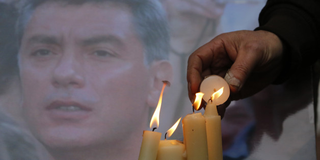 People light candles in memory of Boris Nemtsov, seen behind, at the monument of political prisoners 'Solovetsky Stone' in central St.Petersburg, Russia, Saturday, Feb. 28, 2015. Nemtsov was gunned down Saturday near the Kremlin, just a day before a planned protest against the government. (AP Photo/Dmitry Lovetsky)
