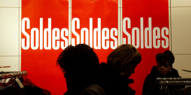 Shoppers look at clothes next to sales posters during the first day of the winter sales in Paris, Wednesday, Jan. 6, 2010. (AP Photo/Christophe Ena)