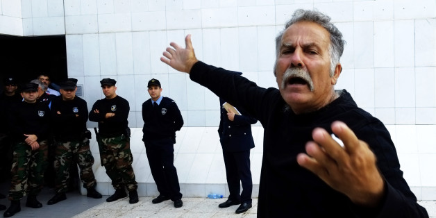 A bondholder shouts as riot police stand guard in front of a main door of Cyprusâ largest lender Bank of Cyprus headquarters in the capital Nicosia, Thursday, Nov. 20, 2014. Several dozen bank bondholders who lost money in Cyprusâ international rescue deal last year staged a protest outside the bankâs headquarters, demanding their money back. Police thwarted some protesters from trying to storm the building during elections for a new bank board of directors. (AP Photo/Petros Karadjias)