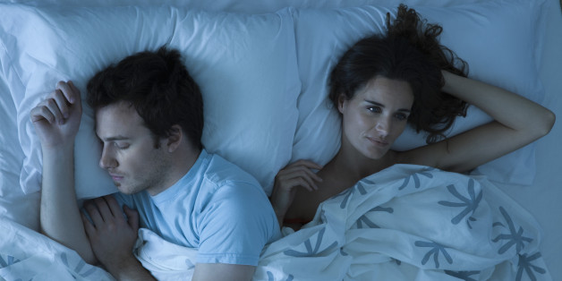 Couple lying together in bed, woman restlessly awake looking away