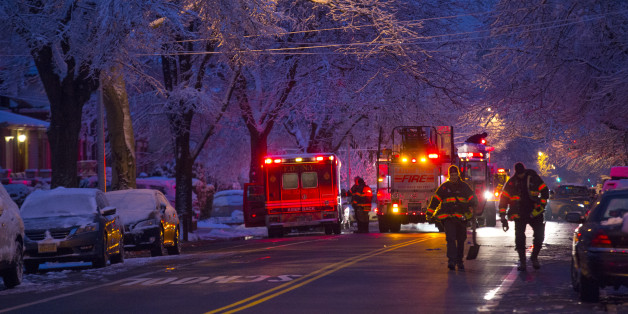 Firefighters walk near the scene of a fire, center left, in which seven children died in the Brooklyn borough of New York Saturday, March 21, 2015. (AP Photo/Craig Ruttle)