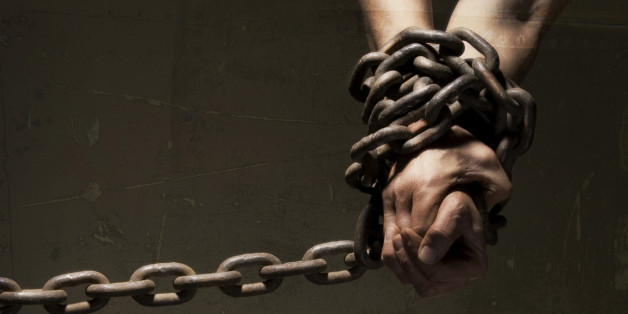 Close-up of wrists and hands bound in heavy metal chains