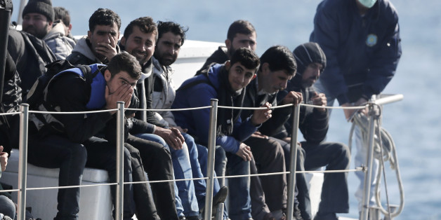 In this Nov. 27, 2014 file photo, a Greek coast guard officer in a mask for fear of infectious disease stands beside a small group of immigrants on a launch taking them to shore from a crippled smuggling ship carrying more than 700 people, at the coastal Cretan port of Ierapetra, Greece. Migrants dreaming of Europe have their pick of social media sites that work like an online travel agent, advertising fares and offering tips on secure payments. Meanwhile, the traffickers who send them floating across the Mediterranean are buying scrapyrd cargo ships over the Internet. (AP Photo/Petros Giannakouris, file)