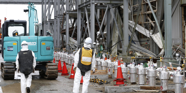 Workers wearing protective gears stand outside the Unit 4 reactor at the Fukushima Dai-ichi nuclear power plant in Okuma, Fukushima prefecture, northeastern Japan, Wednesday, Nov. 12, 2014. More than three years into Japan's massive cleanup of the tsunami-damaged nuclear plant, only a tiny fraction of the workers are focused on the key tasks of dismantling the broken reactors and removing radioactive fuel rods. (AP Photo/Shizuo Kambayashi, Pool)