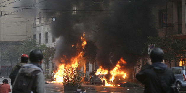 Black smoke billows from a burning car as clashes broke out between demonstrators and police during a protest against the Expo 2015 fair in Milan, Italy, Friday, May 1, 2015. Dozens of people are protesting the opening of Milan's Expo 2015, torching parked cars, smashing bank and store windows and clashing with riot police far from the world's fair sprawling grounds. (AP Photo/Luca Bruno)