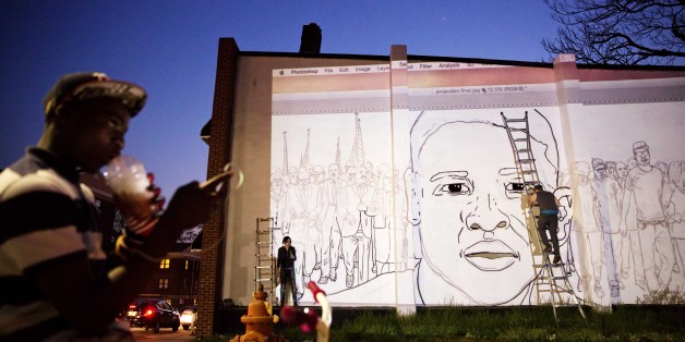 A mural of Freddie Gray is painted on the side of a building by local artist Nether, right, across the street from a makeshift memorial where Gray was arrested Sunday, May 3, 2015, in Baltimore. Baltimore's mayor has lifted a citywide curfew six days after riots were sparked over the death of a Gray who suffered a severe spinal injury while in police custody. (AP Photo/David Goldman)