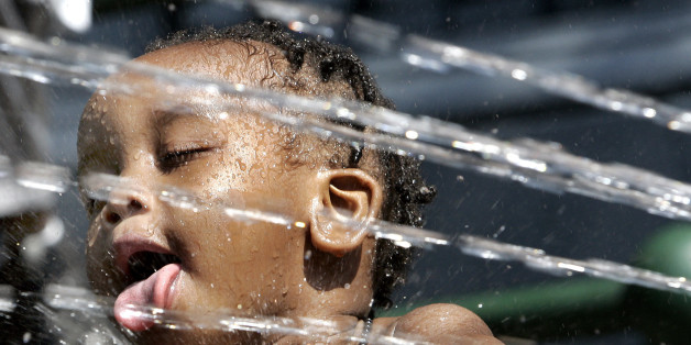 Two-year-old Jaivel Pope gets splashed as he trys to get a drink out of the spray from an open fire hydrant as young kids in Harlem try to beat the heat 01 August 2006 in New York. New York, Boston, Washington, DC, and much of the US East Coast will face record- breaking temperatures that may top 100 degrees(37.7c). The extreme temperatures are also taxing the already strained power system as electrical demand runs high to keep air conditioning running. (Photo credit should read TIMOTHY A. CLARY/AFP/GettyImages)