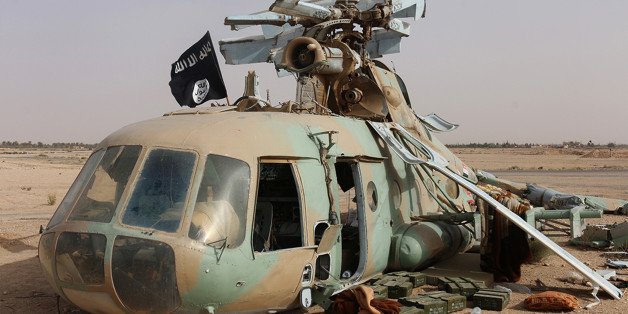 This photo released on Saturday, May 31, 2015 by a militant website, which has been verified and is consistent with other AP reporting, shows a flag of the Islamic State group placed on a damaged helicopter at Tadmur military airbase, which was captured by the Islamic State group in Palmyra in Homs province, Syria. The Syrian military has suffered a series of setbacks in northern Syria recently as insurgents captured the city of Idlib and almost all of Idlib province. The IS group has also seize