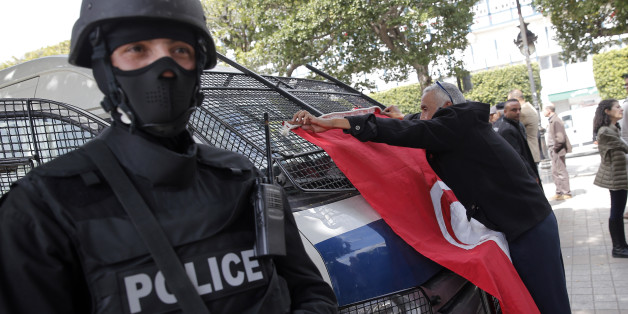 A man places a Tunisian flag onto a police car as a policeman stands guard during a demonstration two days after gunmen attacked the museum and killed scores of people in Tunis, Tunisia, Friday, March 20, 2015. The Islamic State group issued a statement Thursday claiming responsibility for the deadly attack on Tunisia's national museum that killed scores of people, mostly tourists. (AP Photo/Christophe Ena)