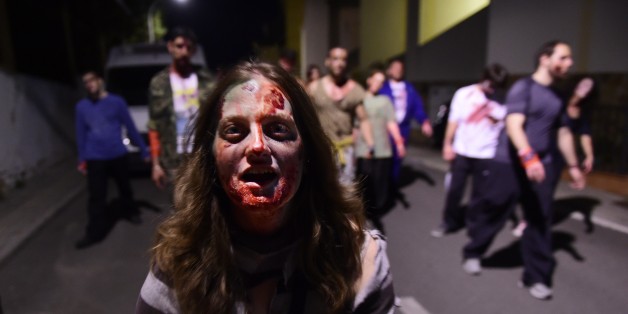 A woman wearing cinema style make-up to resemble the living dead walks along a street followed by a group during the role game 'Survival Zombie' in Olias del Rey on May 30, 2015. Hundred of people gather in Olias del Rey to play in this edition of 'Survival Zombie' that runs from 11pm to 7am and is organised by Spanish company World Real Games. AFP PHOTO / PIERRE-PHILIPPE MARCOU (Photo credit should read PIERRE-PHILIPPE MARCOU/AFP/Getty Images)