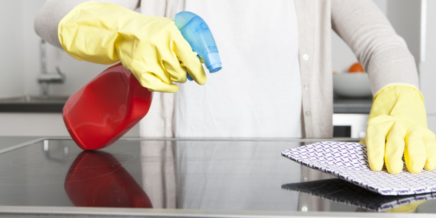 Woman wearing gloves cleaning ceramic glass cooktop with spray