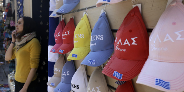 An employee of a tourist shop stands next to caps with the Greek flag in the traditional Plaka district of Athens on Saturday, Feb. 21, 2015. Greece's government starts working on drafting a series of economic reforms it must present to the other euro zone finance ministers on Monday, as part of an agreement reached Friday to extend the country's European loan agreement. (AP Photo/Thanassis Stavrakis)