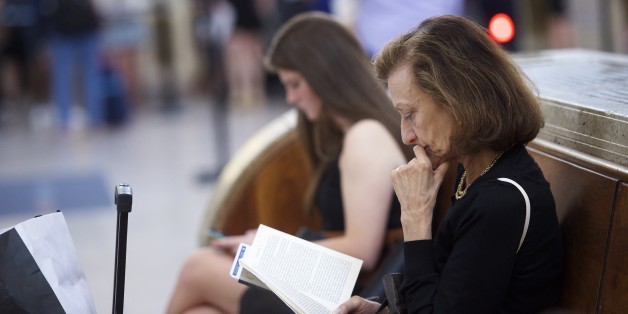 PHILADELPHIA, PA - MAY 18: A woman reads a book while in the background travelers prepare to board their Amtrak train which resumed northbound service from 30th Street Station with a 5:53am departing train, after last week's derailment, on May 18, 2015 in Philadelphia, Pennsylvania. Eight people were killed and more than 200 others were injured in the train crash, carrying more than 200 passengers from Washington, DC to New York, on May 12, 2015 in north Philadelphia. (Photo by Mark Makela/G