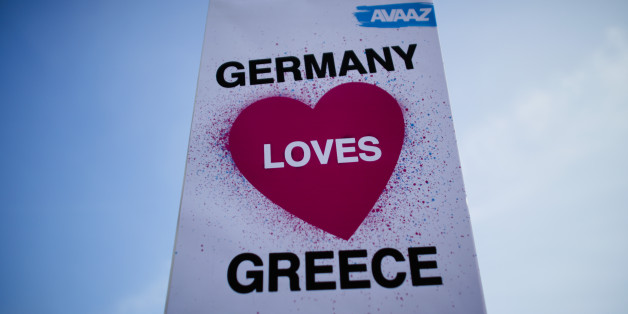 A protestor of the Avaaz organization holds up a poster during a demonstration for German-Greek solidarity prior to a bilateral meeting of German Chancellor Angela Merkel and the Prime Minister of Greece Alexis Tsipras at the chancellery in Berlin, Monday, March 23, 2015. (AP Photo/Markus Schreiber)