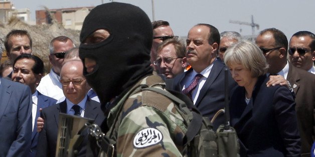 A hooded Tunisian police officer stands guard as British Home Secretary Theresa May, right, Tunisian Interior Minister Mohamed Najem Gharsalli, 2nd right, and French Interior Minister Bernard Cazeneuve, left, pay respect to the victims of Friday's shooting attack on the beach in front of the Imperial Marhaba hotel in the Mediterranean resort of Sousse, Tunisa, Monday, June 29, 2015. Seven people are being interrogated in Tunisia's capital in the investigation into a deadly beach resort attack th