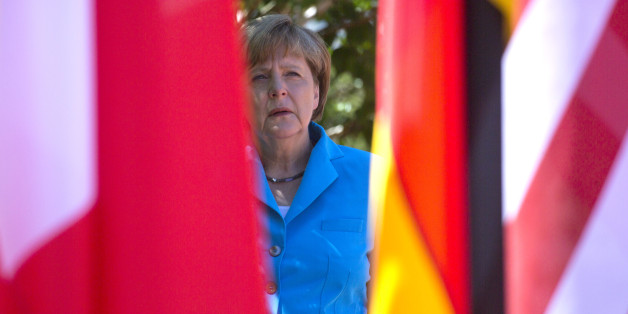 German Chancellor Angela Merkel waits near flags in the shade for G-7 leaders during arrivals for the G-7 summit at Schloss Elmau hotel near Garmisch-Partenkirchen, southern Germany, Sunday, June 7, 2015. The two-day summit will address such issues as climate change, poverty and the situation in Ukraine. (AP Photo/Virginia Mayo)