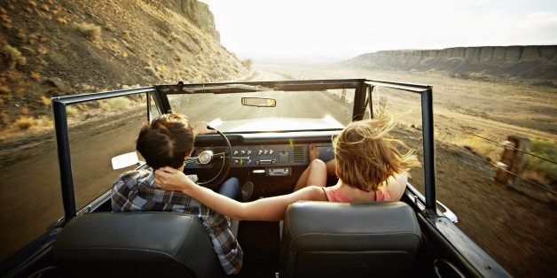 Young couple driving convertible off road vehicle at sunset on desert road