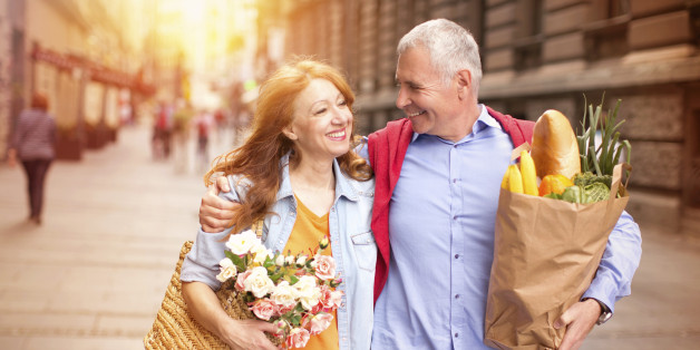 Mature couple outdoors on street with grocery bags.