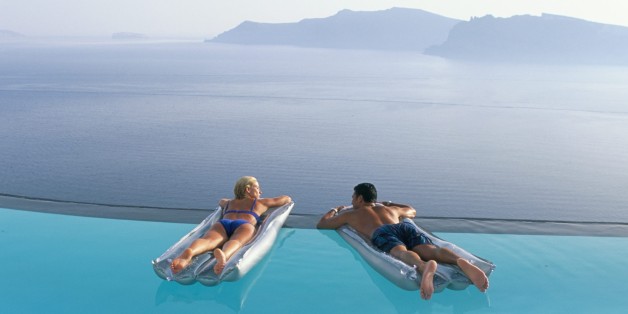 Holidaymakers on lilos in pool looking across bay, Oia, Santorini (Thira), Greek Islands, Greece, Europe