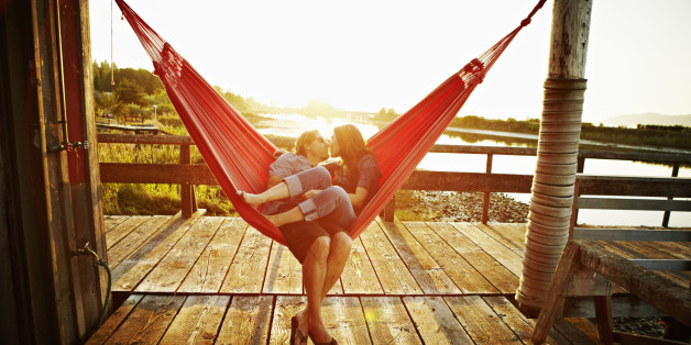 Husband and wife couple kissing in hammock on dock at sunset
