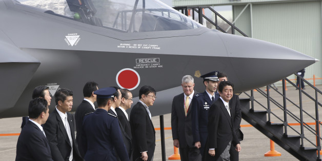 FILE - In this Oct. 26, 2014 file photo, Japanese Prime Minister Shinzo Abe, right, walks by a mock-up of the F-35 fighter jet during the annual Self-Defense Forces Commencement of Air Review at Hyakuri Air Base, north of Tokyo. Japan emphasized China as a threat in escalating regional tensions in this year's annual defense report, approved Tuesday, July 21, 2015 by the Cabinet, as Abe's government tries to convince the public of the need to pass legislation to give Japan's military a greater ro