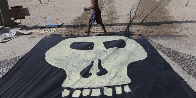 A man walks past a banner with a drawing of a skull symbolizing the death of nature during a protest on the Copacabana beach in Rio de Janeiro, Brazil, Saturday, Aug. 1, 2015. Less than a dozen people showed up for a scheduled protest by environmentalists against the money spent in preparation for the Olympics and the construction of the game's golf course that was partially carved out of a nature reserve. (AP Photo/Silvia Izquierdo)