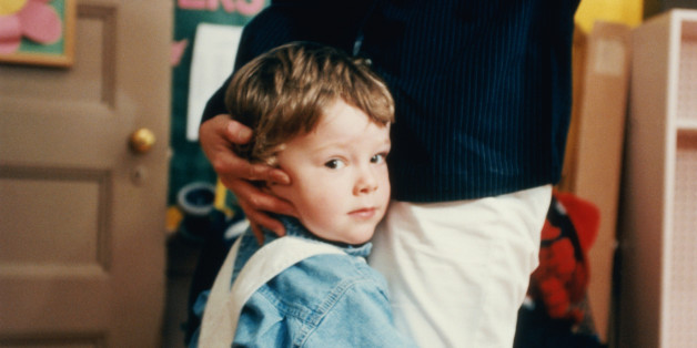 Boy (4-6) embracing mother's leg in classroom, portrait