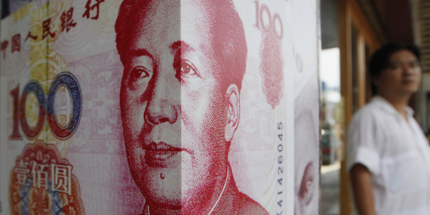 A man stands next to a copy of the Chinese RMB at a money exchange store in Hong Kong Friday, July 20, 2012. (AP Photo/Kin Cheung)