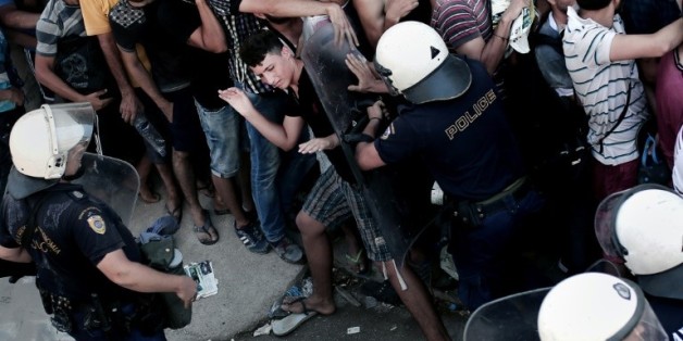 Un policier pousse des migrants qui font la queue et attendent leur prise en charge administrative dans le stade de l'île de Kos, le 12 août 2015