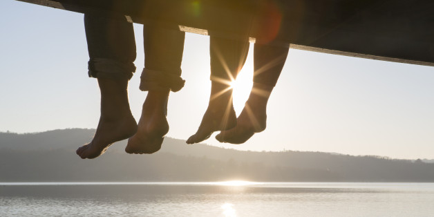 Couple's feet dangle from dock,above tranquil lake