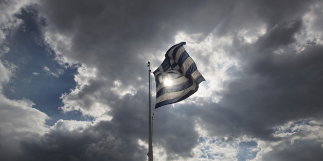 Tourists stand beneath a Greek flag fluttering against the sun at the ancient Acropolis hill , in Athens, on Monday June 22, 2015. A top European Union official said that debt talks between Greece and its international creditors have made some progress but that a deal to avoid potential bankruptcy remains elusive. (AP Photo/Petros Giannakouris)