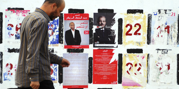 In this photo taken Wednesday, Nov. 5, 2014, a man walks past electoral posters for the upcoming presidential elections in Tunis. Campaign posters and banners for next weekâs presidential elections have covered the walls of Tunisiaâs cities and towns, papering over the flaking posters from the parliamentary elections just three weeks ago. (AP Photo/Hassene Dridi)