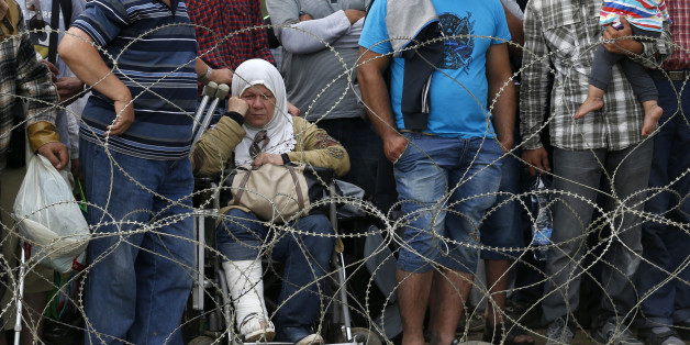 Migrants stand behind the barbed wire set by Macedonian police to stop thousands of migrants entering Macedonia illegally from Greece near the southern Macedonian town of Gevgelija, Saturday, Aug. 22, 2015. About 39,000 people, mostly Syrian migrants, have been registered as passing through Macedonia in the past month, twice as many as the month before. (AP Photo/Darko Vojinovic)