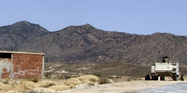 FILE - In this June 25, 2013 file photo, a Tunisian armored personnel carrier patrols near the Jebel Chaambi mountain. Writing on building at left reads: "For Sale". Militants in eastern Tunisia staged two simultaneous attacks on army posts while soldiers held a Ramadan feast, killing at least 14 soldiers, authorities said Thursday July 17, 2014. An extremist group believed linked to al-Qaida's North Africa arm claimed responsibility for the attacks on Mount Chaambi on its Facebook page, calling