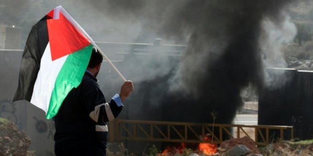 Un manifestant palestinien brandit le drapeau national et regarde des pneus bruler près de la barrière de séparation israélienne, le 14 janvier 2011, dans le village de Nilin à l'ouest de Ramallah