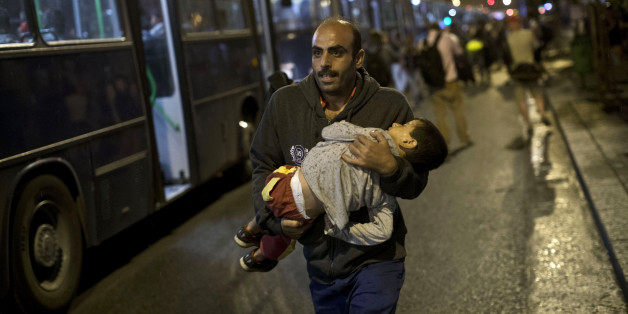 A man runs with child in arms as he tries to board a bus provided by Hungarian authorities for migrants and refugees at Keleti train station in Budapest, Hungary, Saturday, Sept. 5, 2015. Hundreds of migrants boarded buses provided by Hungary's government as Austria in the early-morning hours said it and Germany would let them in. Austrian Chancellor Werner Faymann announced the decision early Saturday after speaking with Angela Merkel, his German counterpart - not long after Hungary's surprise