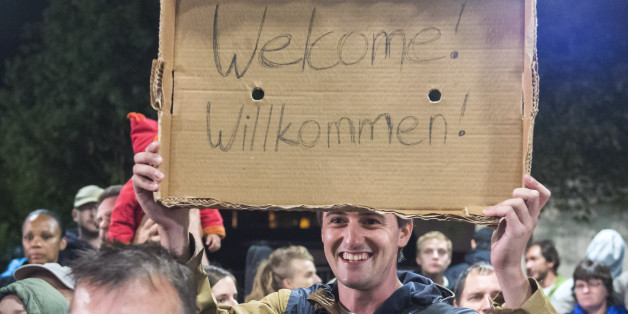Am man holds a cardboard with a 'Welcome' slogan during the arrival of refugees at the train station in Saalfeld, central Germany, Saturday, Sept. 5, 2015. Hundreds of refugees arrived in a train from Munich to be transported by busses to an accomodation centre. (AP Photo/Jens Meyer)