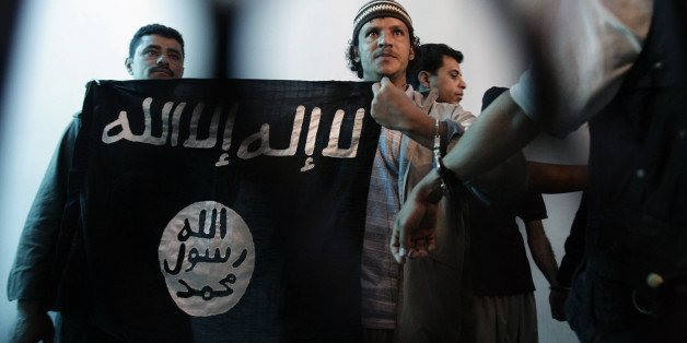 FILE - In this April 23, 2013 file photo, a suspected Yemeni al-Qaida militant, center, holds a banner as he stands behind bars during a court hearing in state security court in Sanaa, Yemen. In a competition with the Islamic State group for recruits and prestige across the Middle East, al-Qaida has sought to distinguish itself from its rival's bloodthirstiness, taking an approach that in jihadi circles would be considered pragmatic. (AP Photo/Hani Mohammed, File)