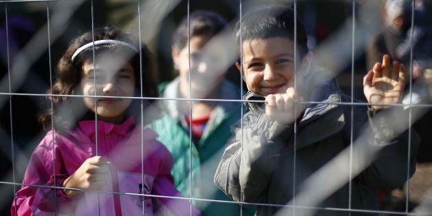 Children smile into the camera behind a fence in a temporary holding center for migrants near the border line between Serbia and Hungary in Roszke, southern Hungary in Roszke, Saturday, Sept. 12, 2015. Hundreds of thousands of Syrian refugees and others are still making their way slowly across Europe, seeking shelter where they can, taking a bus or a train where one is available, walking where it isn't. The latest string of walkers made their way Friday from the Hungarian border across Austria t